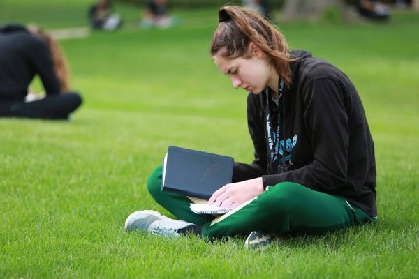 girl sitting cross-legged on the grass with a book and paper