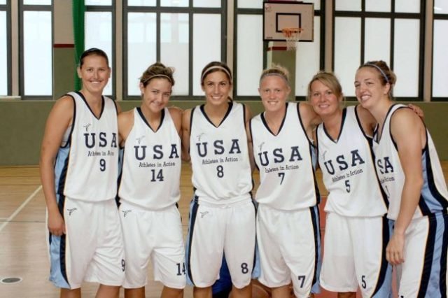 6 women posing together for a photo, all wearing white USA uniforms.