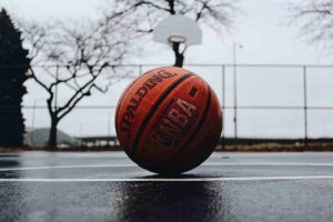 A basketball sitting on an outside court that looks wet.