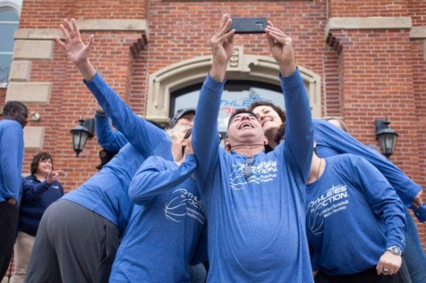 Several people in blue basketball shirts looking up at a phone, taking a selfie.