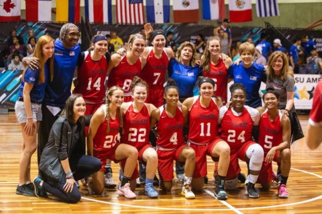 Group picture being taken of a women's basketball team on a court wearing red uniforms