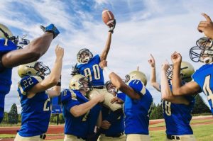 Young football team celebrating by holding up the player who is holding the football high