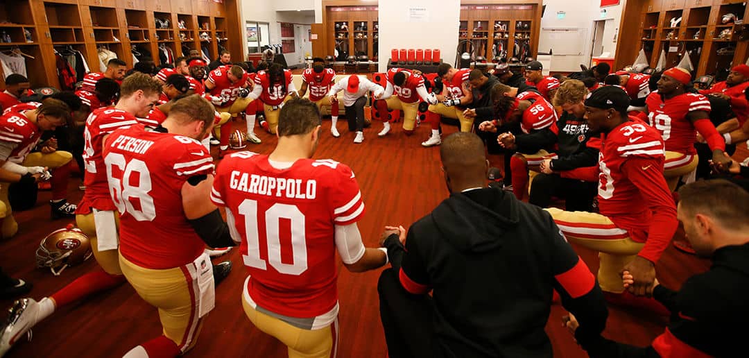 Pro football players and chaplains praying together in a circle