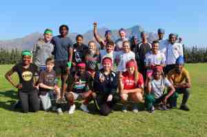 Group of athletes posing in front of mountainsin front of mountainsfor a picture with their index fingers pointing to the sky