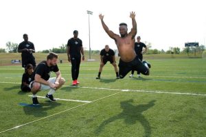 Man jumping forward on field while others watch