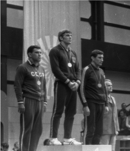 Black and white photo of three men on podiums with medals around their necks