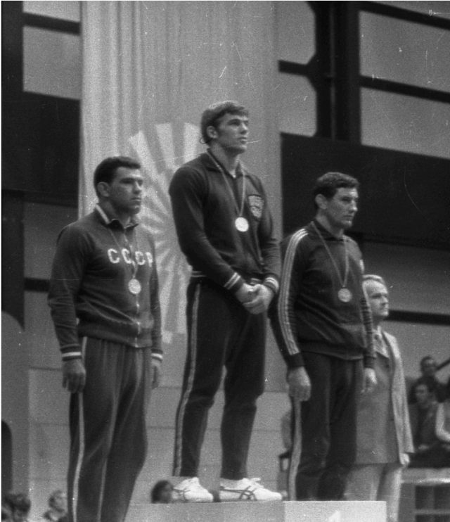 Black and white photo of three men on podiums with medals around their necks