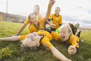 girl athletes celebrating in dog pile on the ground