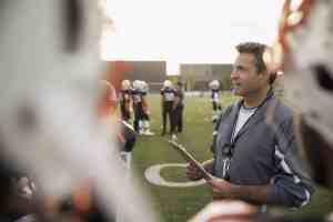 Coach with clipboard talking to high school football team on football field