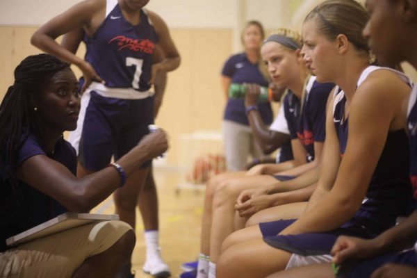 A woman squatting down and giving instructions to a team of women on the sideline of a court