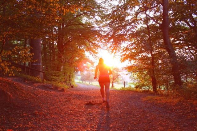 girl running on trail between trees toward the sun.