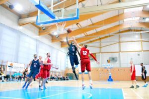basketball player in midair to put the basketball in the net over 2 players in red