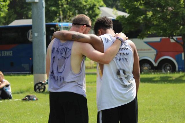 Back of two athletes on a field with arms around each other's shoulders and heads bowed.