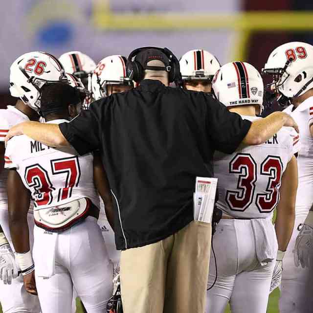 Back of man with arms around shoulders of football players in a huddle