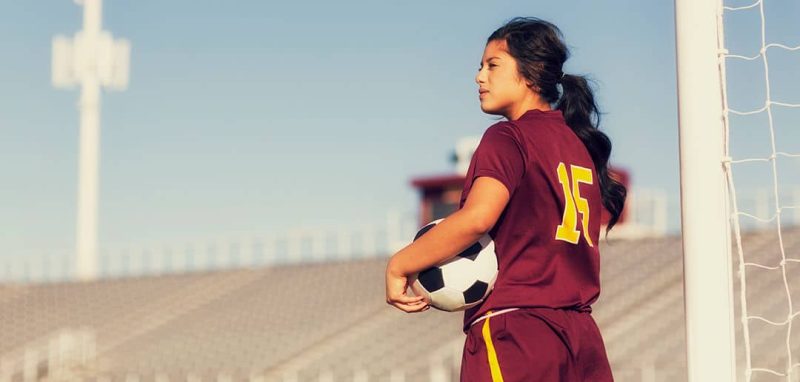 girl holding soccer ball, staring out over a field