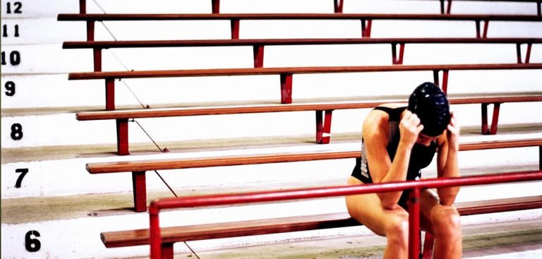 swimmer sitting on bleachers with head in hands