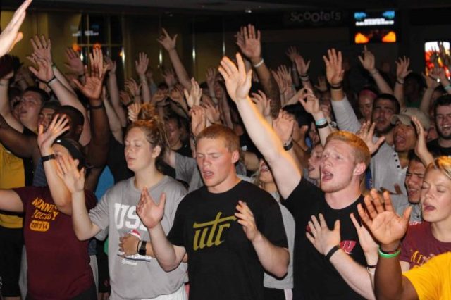 large group of young men and women with hands raised, singing
