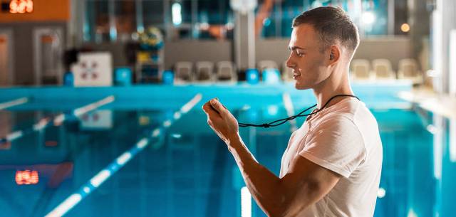 swimming coach standing at edge of pool looking at whistle
