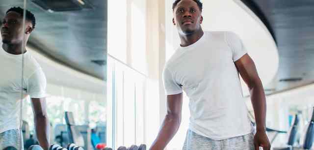 Man standing next to mirror in weight room gripping hand weight