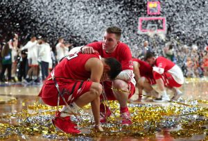 Two men in red uniforms squatting down on basketball court with confetti all around