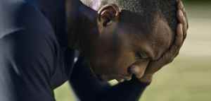 Close up of a man leaning over with one hand on head, looking down on a green field