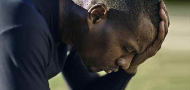 Close up of a man leaning over with one hand on head, looking down on a green field