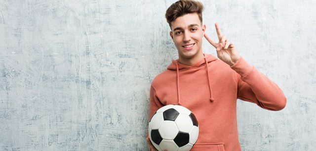 young man holding a soccer ball and making a 'v' sign with two fingers