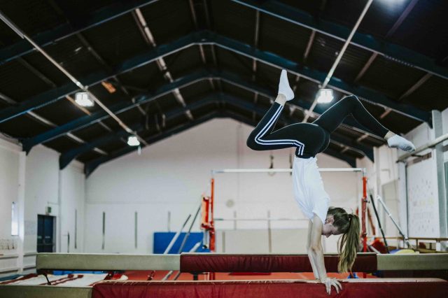 Female gymnast doing a handstand on a balance beam