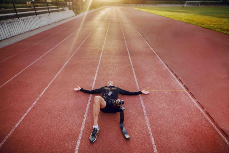 young athlete with artificial leg lying on racetrack