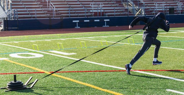 Athlete pulling sled with weights on turf field in cold weather