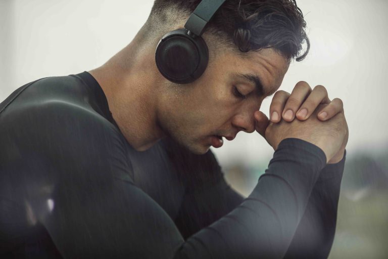 Young man wearing black headphones with eyes closed praying