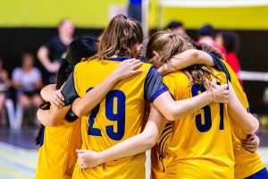 Female volleyball players in yellow uniform huddling together before starting the game