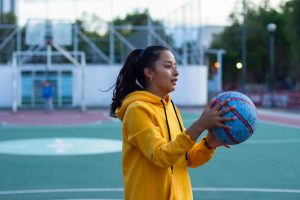 Young woman athlete in a yellow hoodie holding a blue basketball