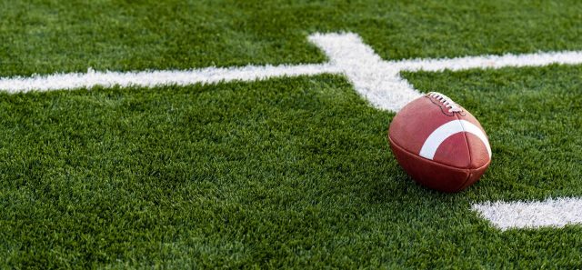 A brown leather american football on a green playing field
