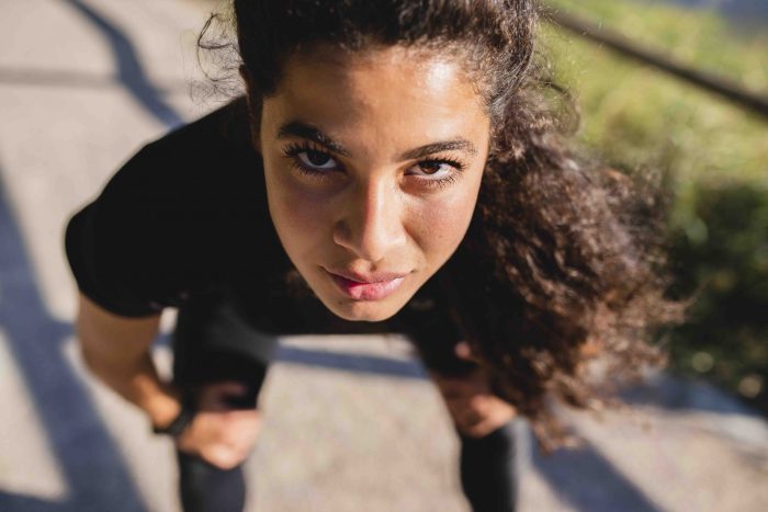 closeup of girl's intense face looking at camera from a bent-over position ready to spring forward on a road.