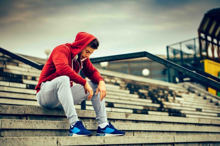 Young man resting on the stairs after running lone athlete sitting in bleachers looking down