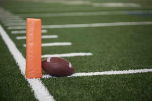 American football resting on field next to orange marker