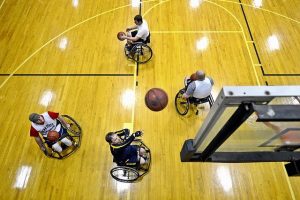 male wheelchair basketball players on a court, one is throwing the ball up toward the backboard