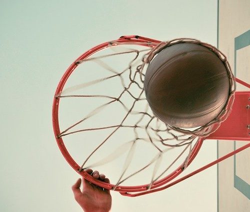 Looking up at hand on basketball rim, ball dropping through the net
