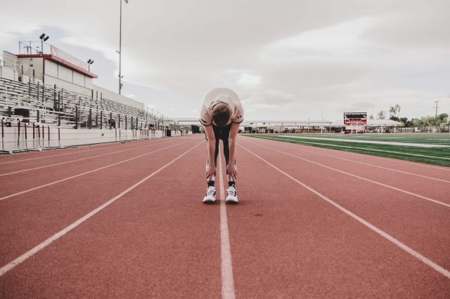Facing an athlete bent over at the waist looking down in the middle of a track.