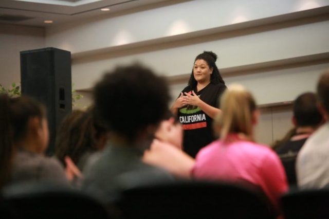 Woman standing and talking to audience seated before her
