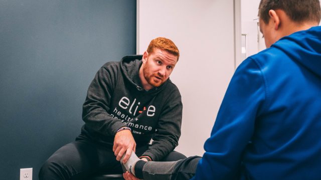 man in black and white hoodie checking an athlete's foot.