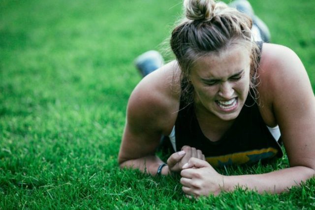 Girl laying on grass with a grimacing expression