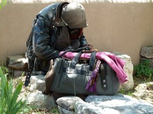 homeless person with head bowed and belongings around him