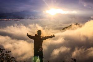 Back of silhouette of a man in front of clouds and the sun.