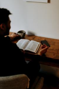 Looking over the shoulder of a shadowy man reading a Bible at a desk.
