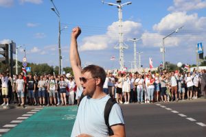 Young man with hand raised in a fist, standing on a road with a large group of racers beside him on the road to begin a race.