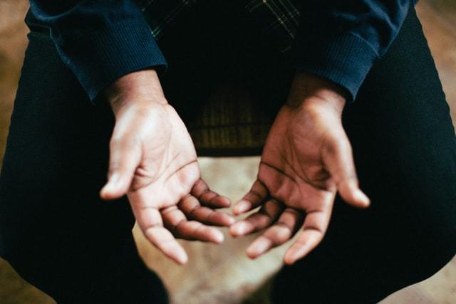 Two hands of seated person in black with palms up above legs