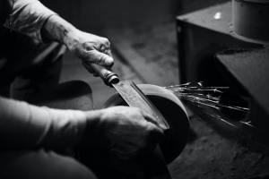 knife blade being sharpened on a wheel in black and white
