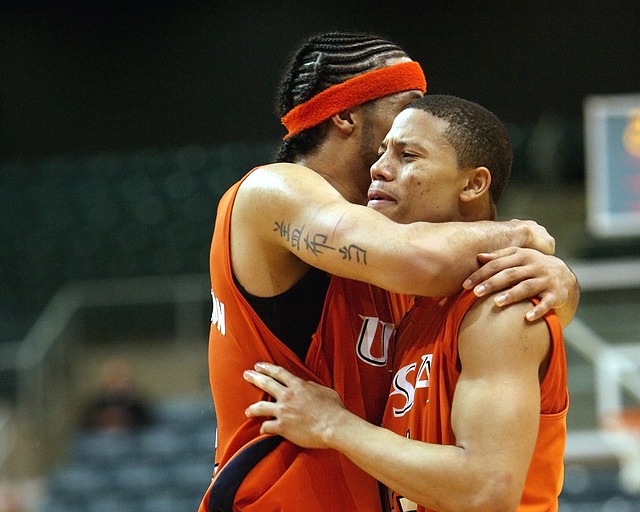 One man hugging another, both in red basketball uniforms